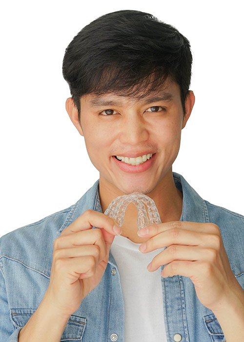 Smiling Asian man holding clear aligners